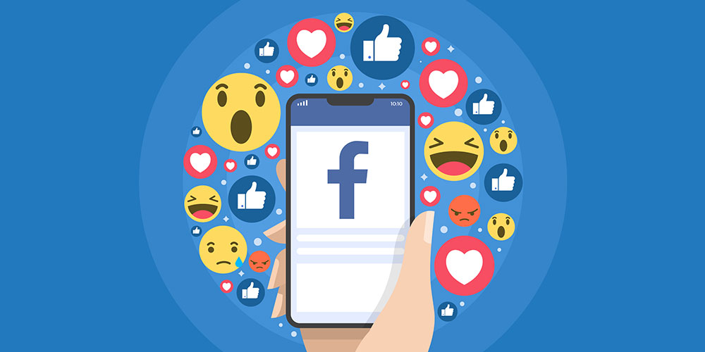 Ilustrasi tangan yang memegang ponsel dengan Facebook terbuka, emoji reaksi Facebook mengelilingi ponsel